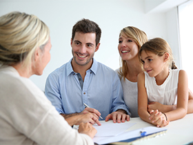 Family of four discusses documents with a professional at a table, smiling during a planning session.